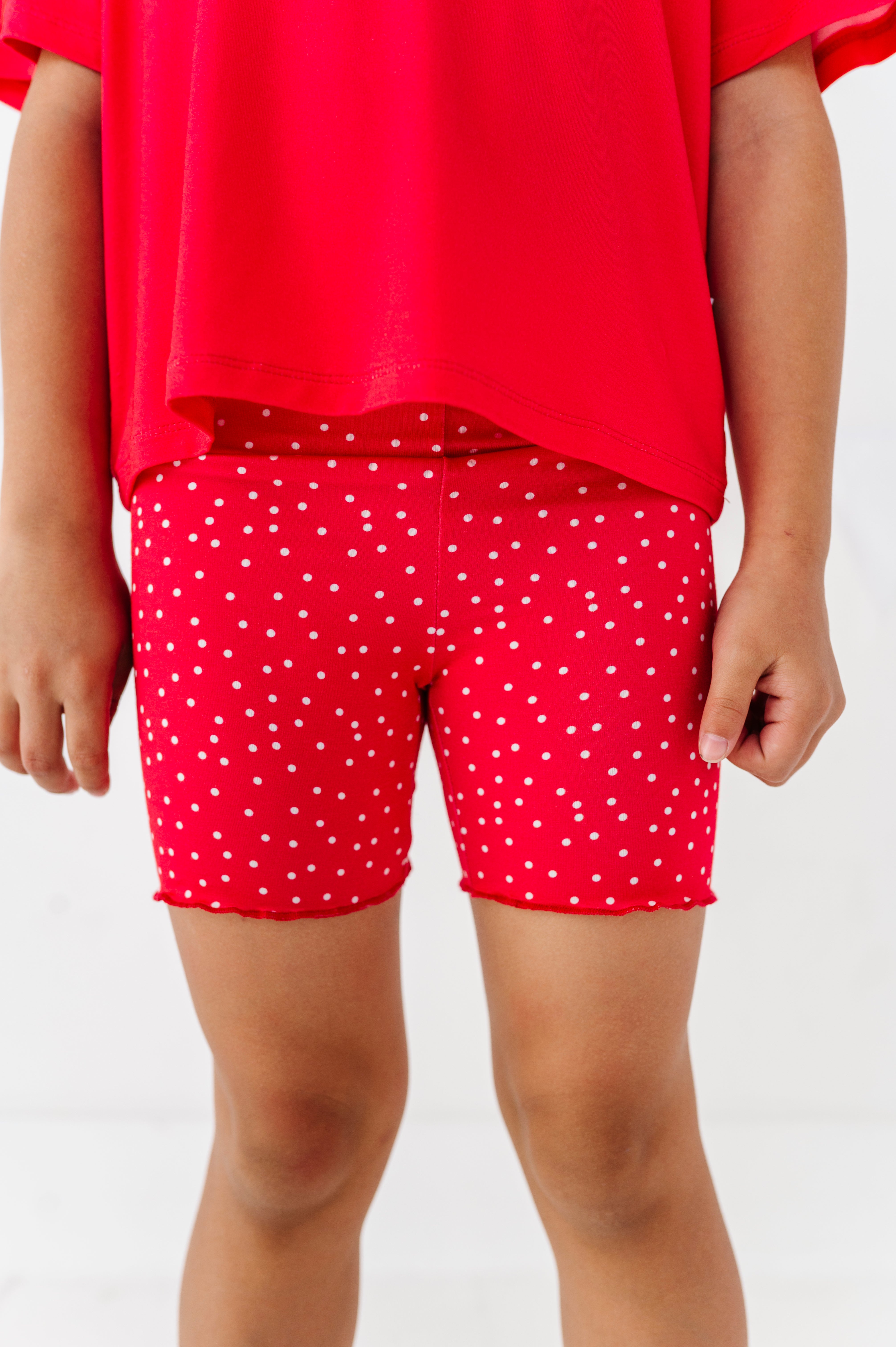 Person wearing red polka dot shorts and a red top on a white background